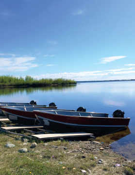 Picture of a lake, there are four 12 foot boats in the foreground resting on the beach.
