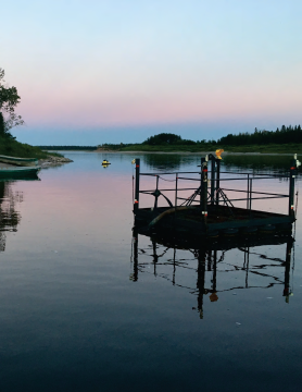 Picture of lake during the evening. There is a yellow sea-doo in the background and a water collection station in the foreground located in the water.