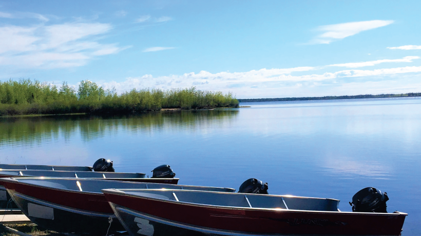 Picture of a lake, there are four 12 foot boats in the foreground resting on the beach.