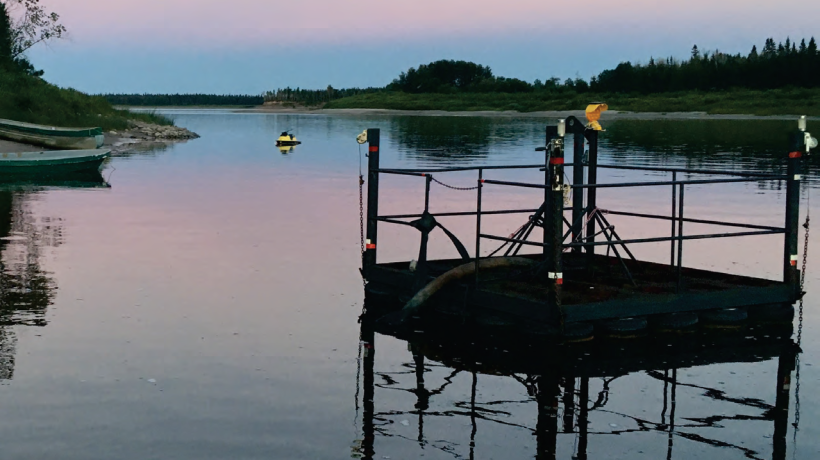 Picture of lake during the evening. There is a yellow sea-doo in the background and a water collection station in the foreground located in the water.